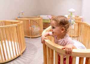 A joyous toddler is playing happily in a stylish nursery filled with wooden cribs and modern design